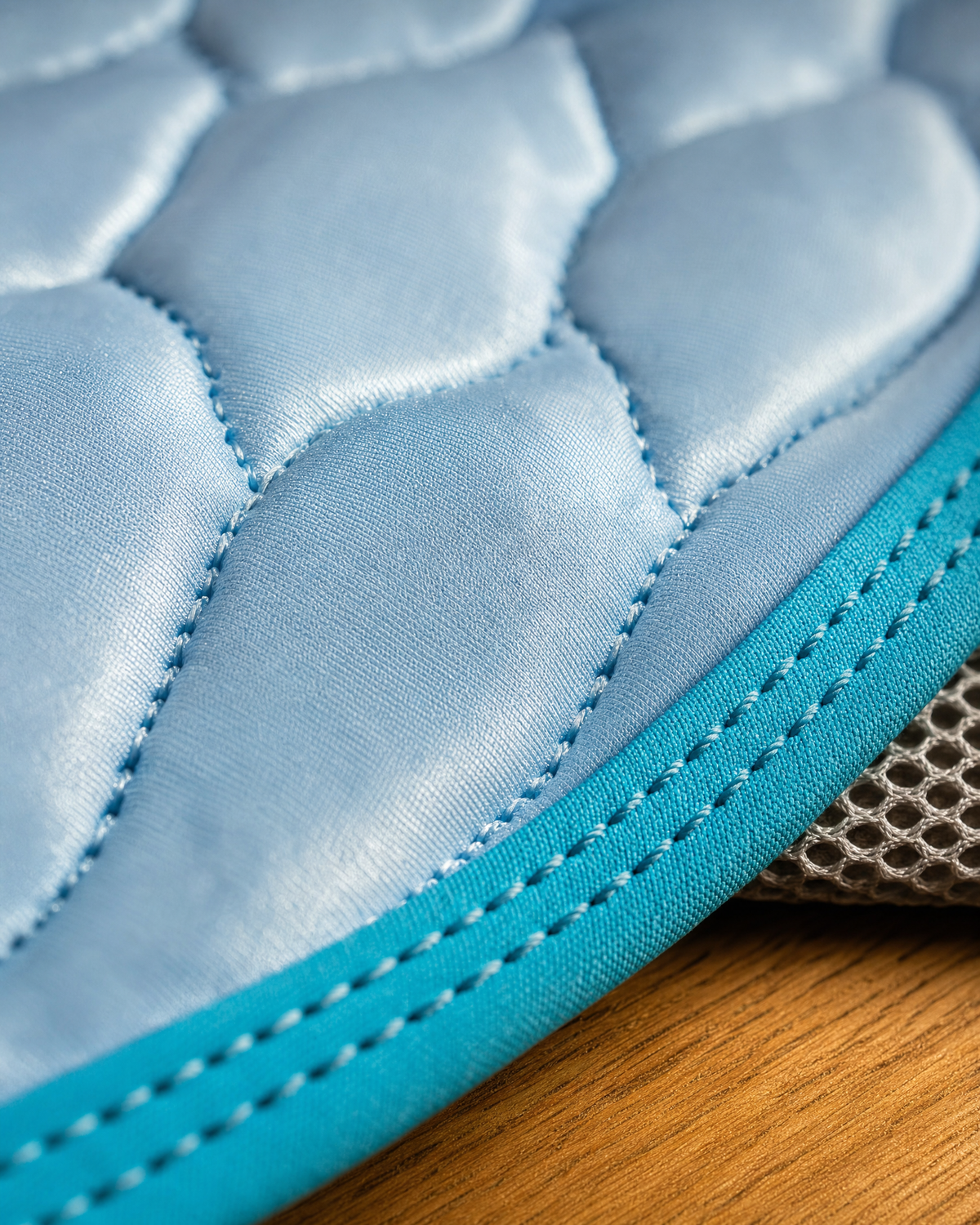 Macro of the quilted ice-silk surface, the cyan bound edge stitching and the grey mesh backing
